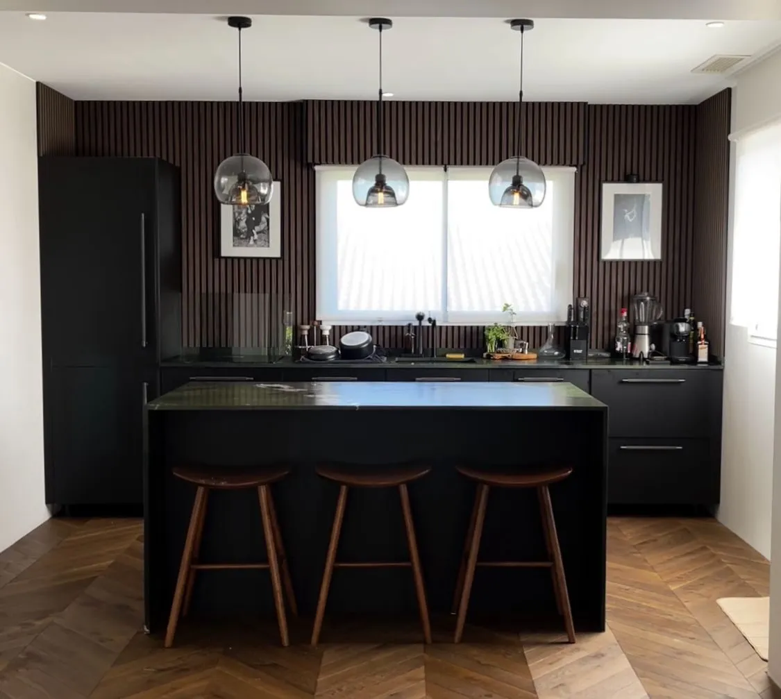 Cuisine ouverte noire avec îlot central, tabourets bois et verrière
